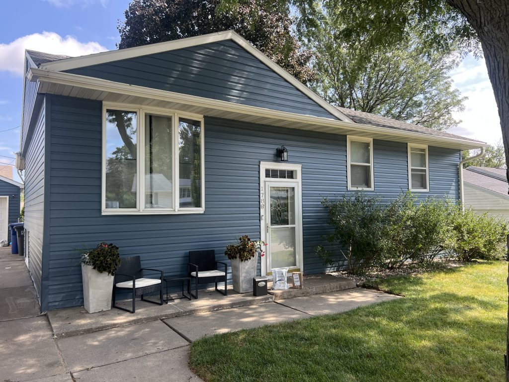Painter pressure washing and prepping weathered exterior siding before repainting a Cascade home